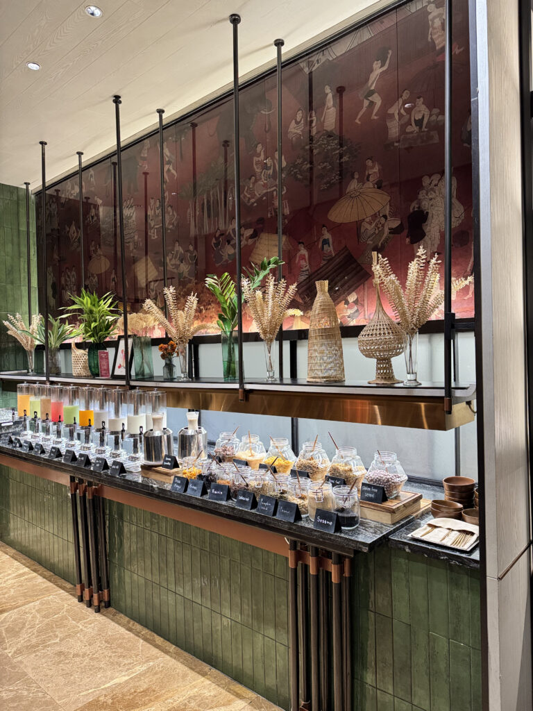 Dispensers and glass jars lined up beneath the Lanna mural