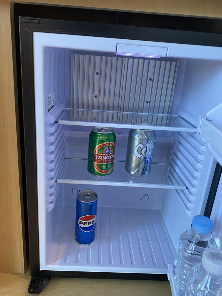 The minibar fridge. Tsingtao, Cass, Pepsi, and water, one round free