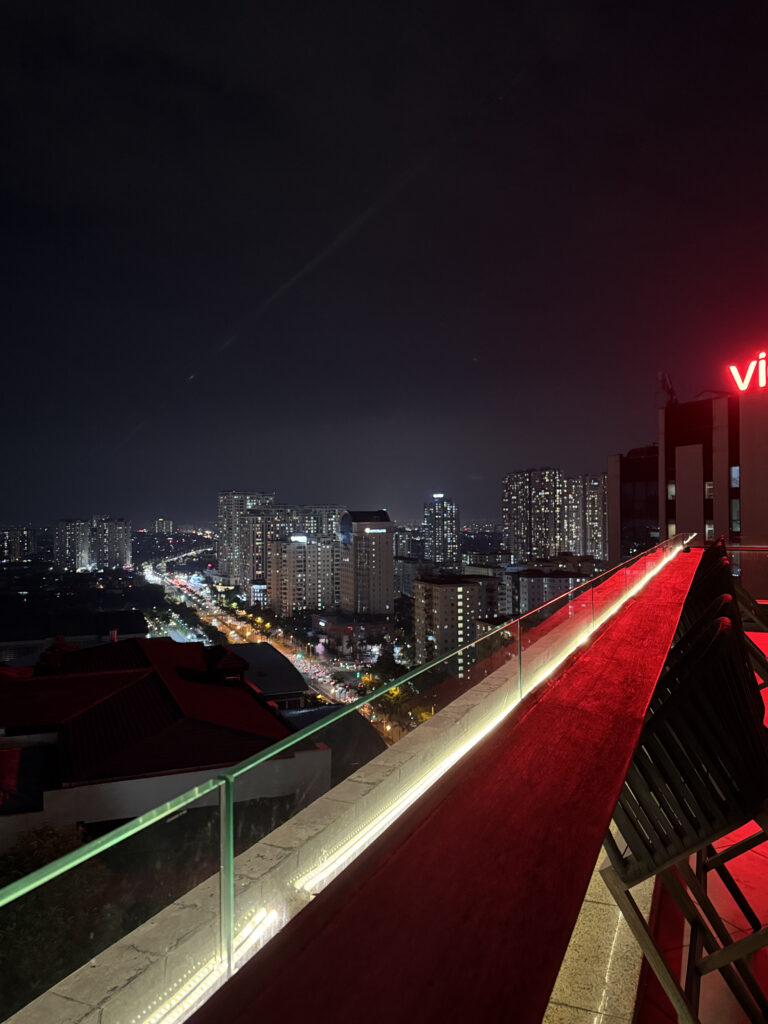 The rooftop deck at night. Red light across the deck, Hanoi glowing below
