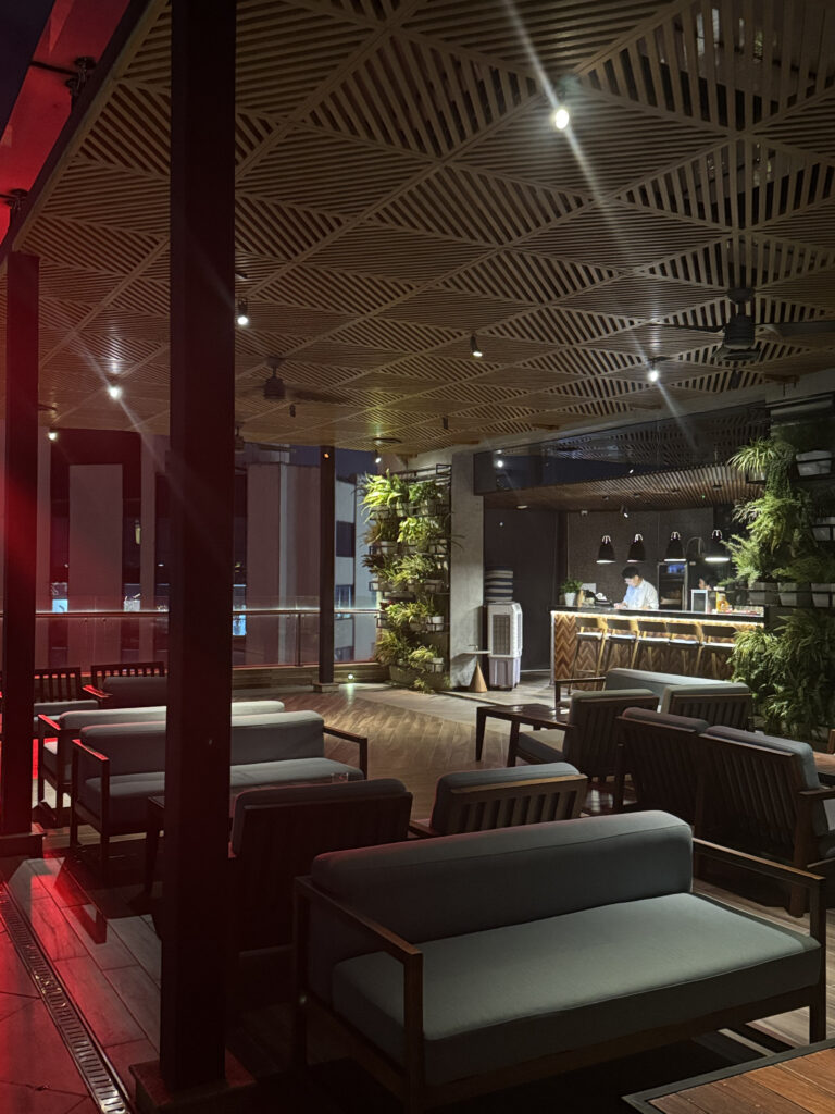 Inside the sky bar. Sofa seating, the bar counter, and the wooden ceiling louvers